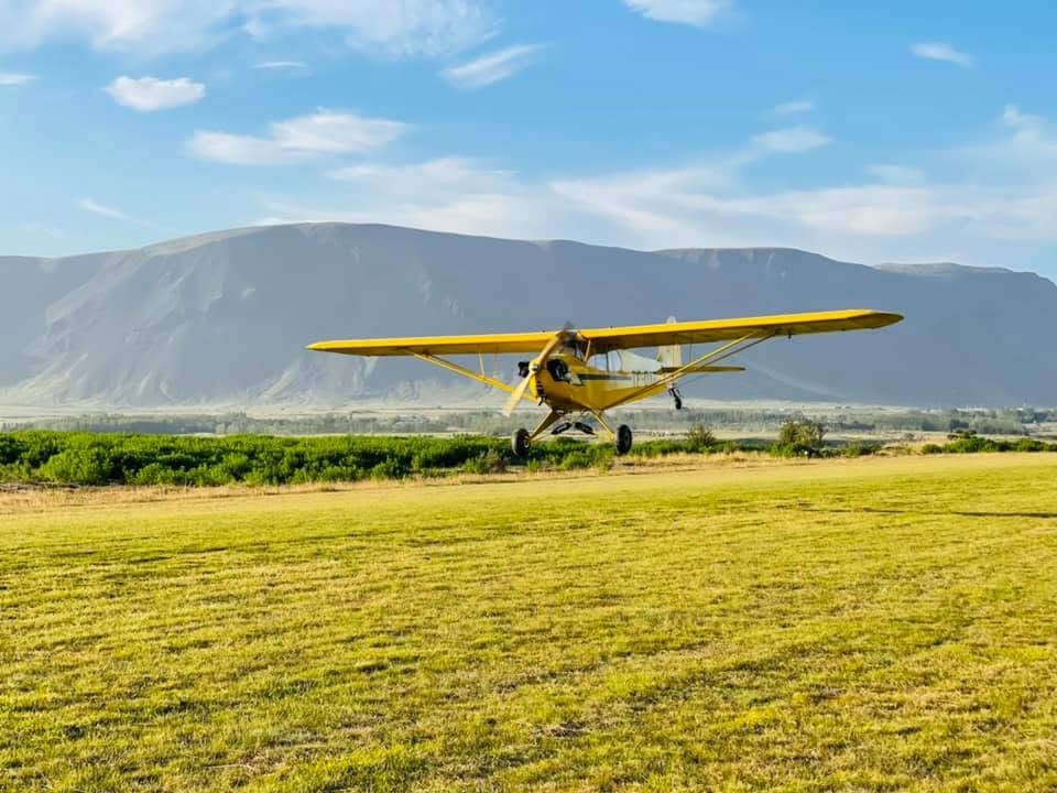 Gul Piper Cub flugvél á grasflugbraut við Selfoss með fjöll í baksýn