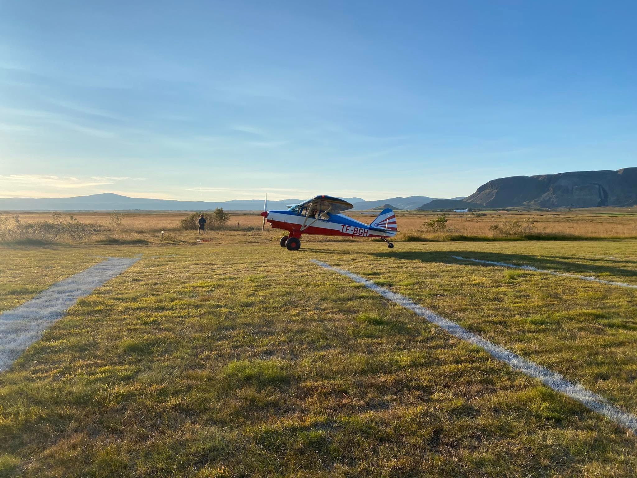 Rauð-hvít-blá flugvél TF-BGH á grasflugbraut Selfossflugvallar í kvöldsól